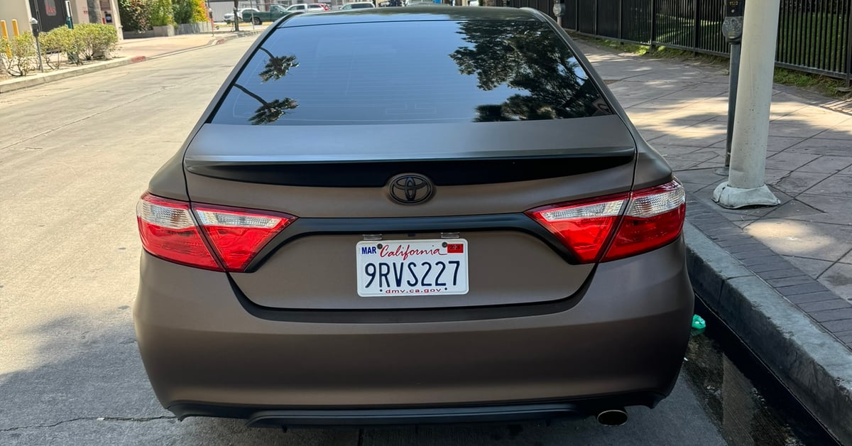 Rear view of a Toyota Camry with a custom matte brown vinyl wrap parked on a street in Los Angeles.